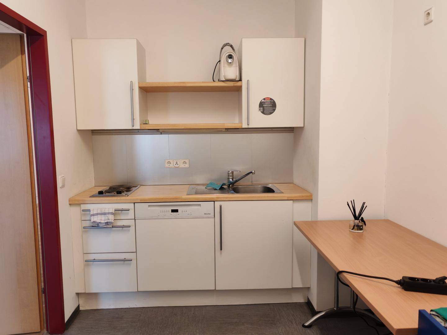 Kleine Küchenzeile mit Spüle, Kochfeld, Geschirrspüler und Hängeschränken, ideal für kompakte Wohnlösungen.