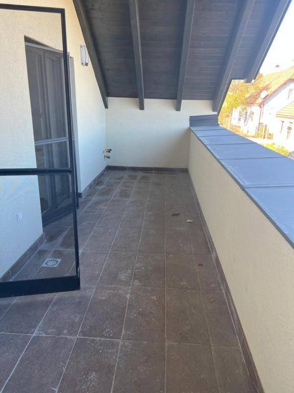 Leerer Balkon mit Fliesenboden und sichtbaren Holzbalken unter dem Dach.