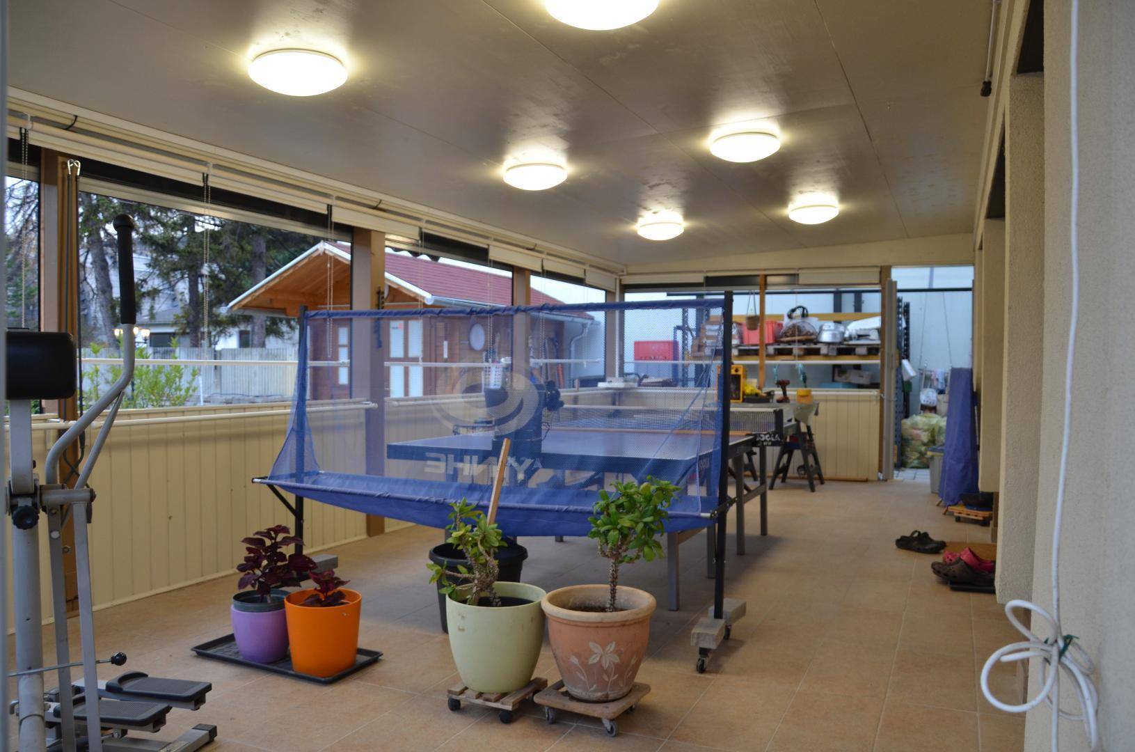 Überdachter Außenbereich, möglicherweise ein Wintergarten, mit Tischtennisplatte und Fitnessgeräten.