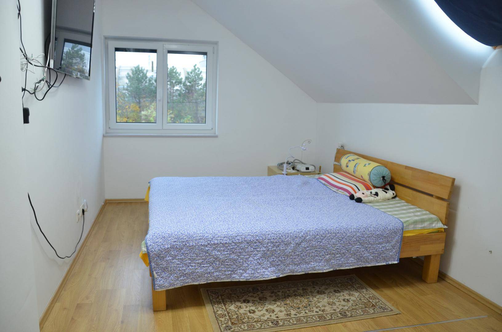 Schlafzimmer mit Doppelbett, Wandfernseher und Fenster unter einer Dachschräge.