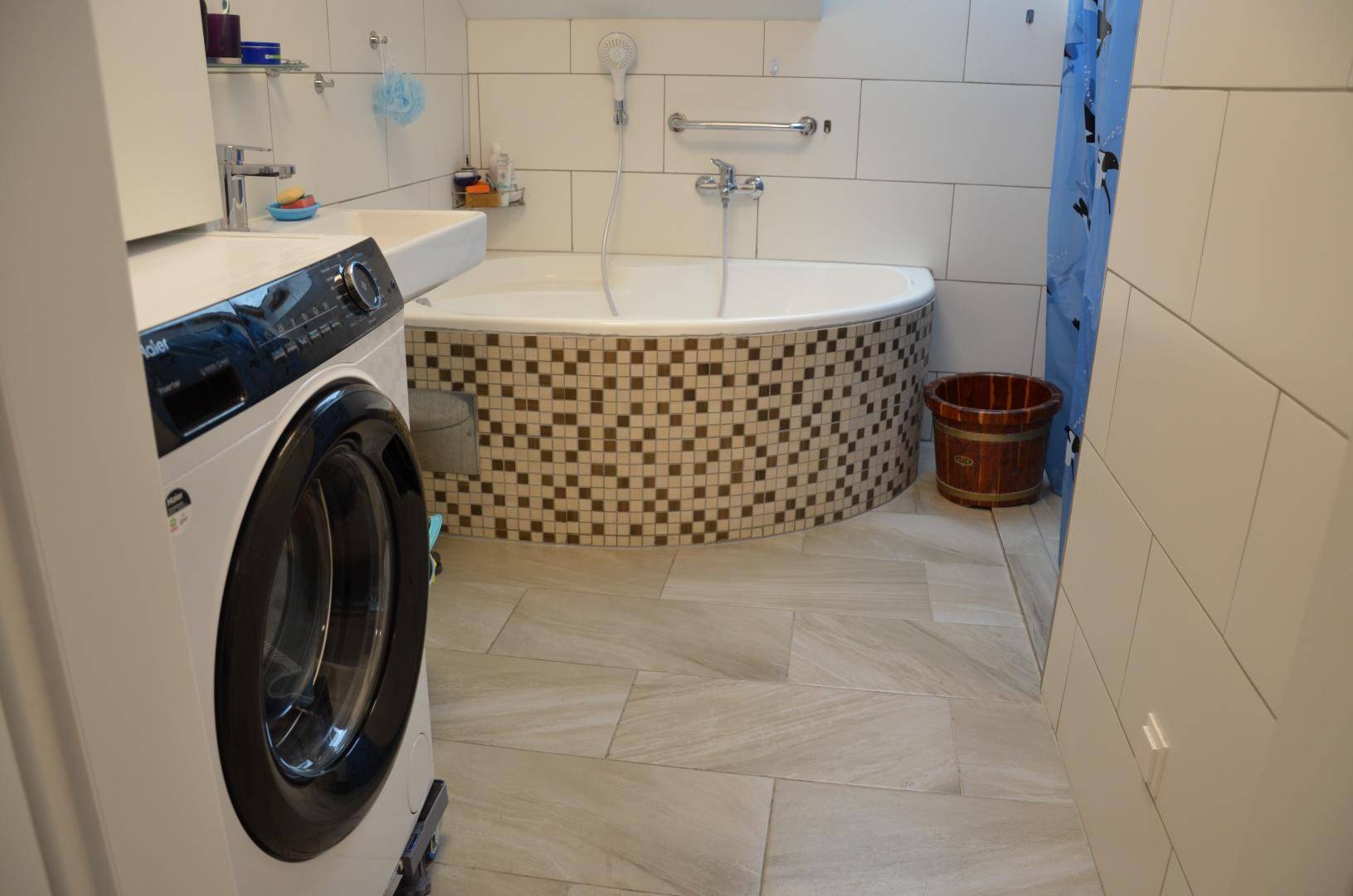 Badezimmer mit Waschmaschine, Eckbadewanne mit Mosaikfliesen und hellen Wandfliesen.
