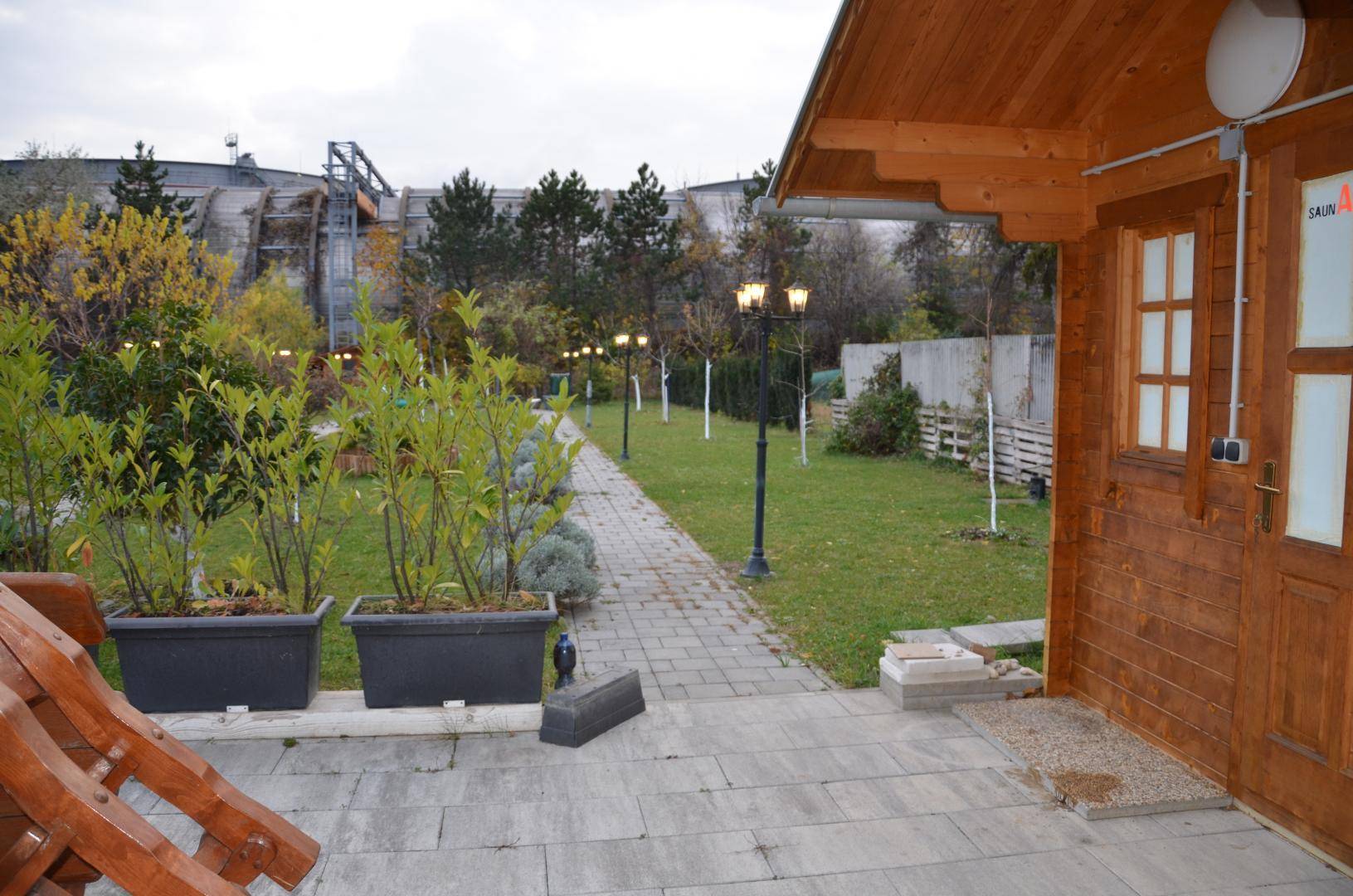 Gartenbereich mit Holzsaunahaus, gepflastertem Weg und Bäumen im Hintergrund.