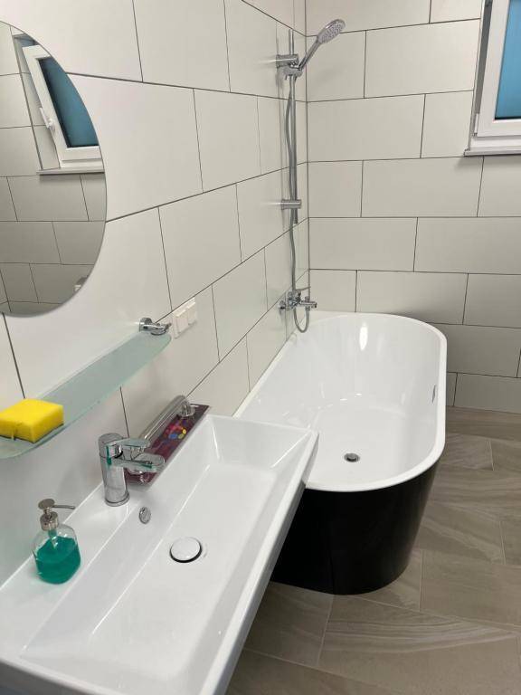 Modernes Badezimmer mit freistehender Badewanne, rechteckigem Waschbecken und weißen Wandfliesen.