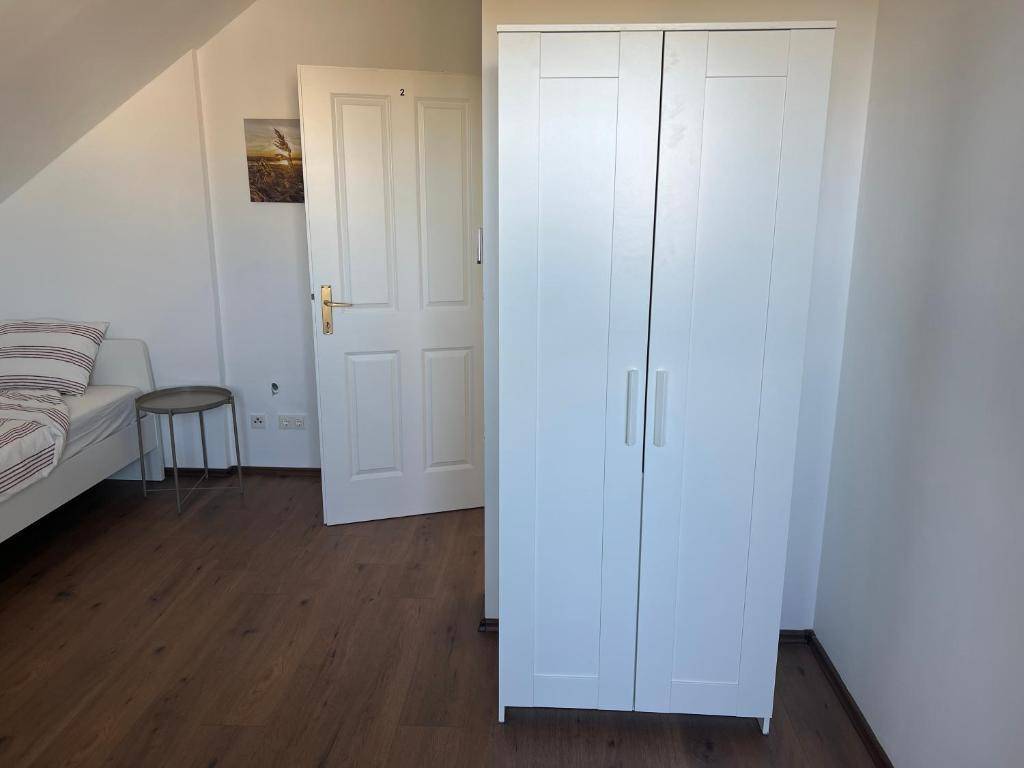 Teil eines Schlafzimmers mit weißem Kleiderschrank und Tür, unter einer Dachschräge gelegen.