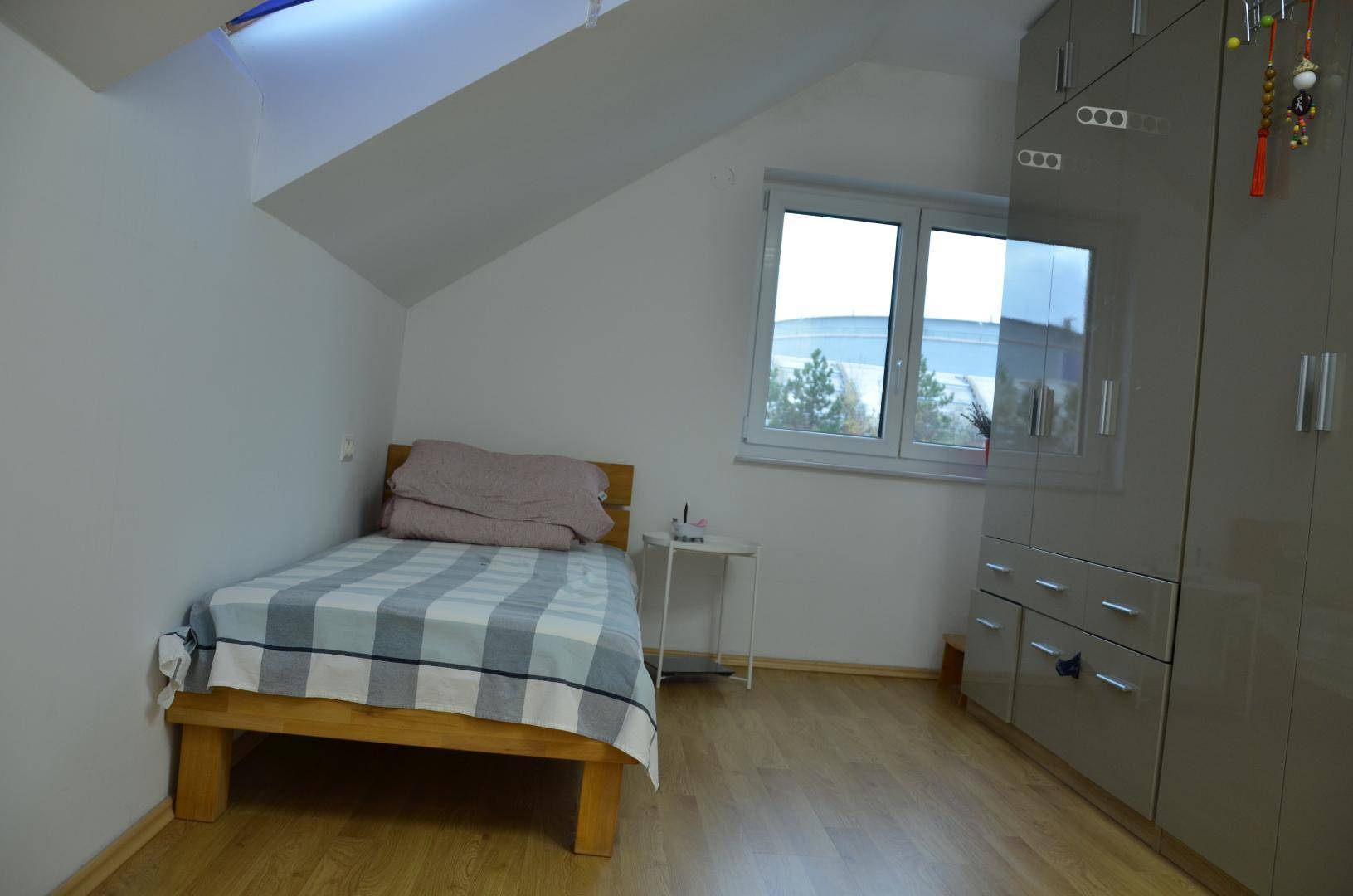 Schlafzimmer mit Einzelbett, grauem Kleiderschrank und Fenster unter einer Dachschräge.
