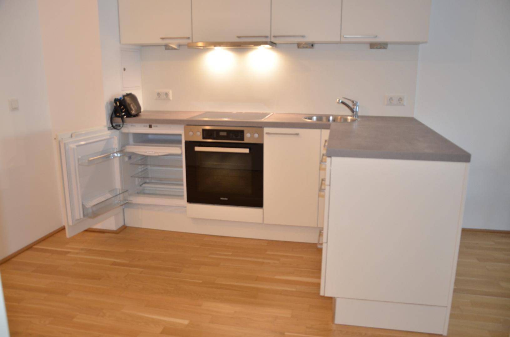 Kompakte Einbauküche mit modernen Geräten, Spüle und integriertem Kühlschrank.