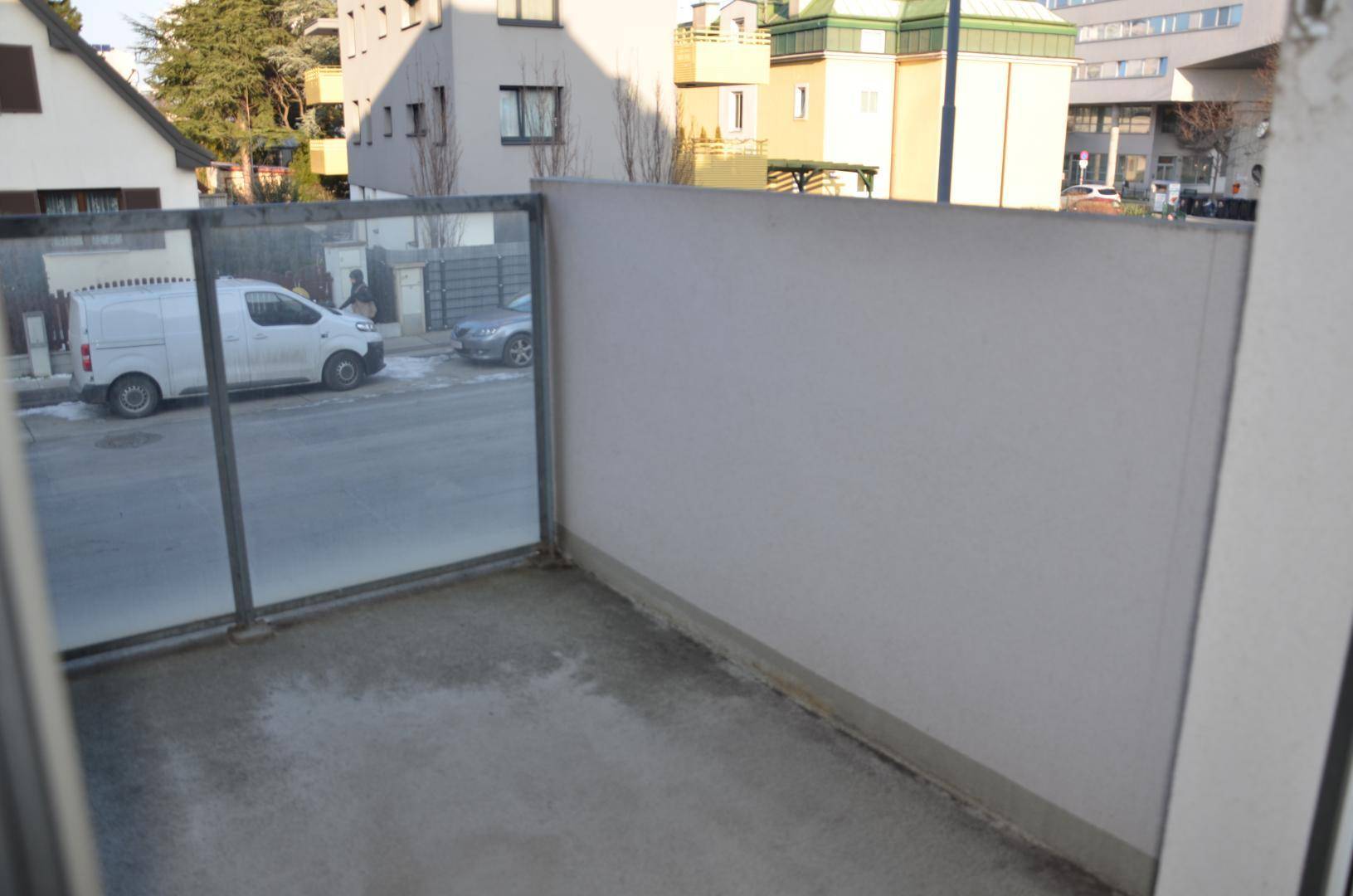 Balkon mit moderner Glasbrüstung und Ausblick auf die Straße und Nachbargebäude.