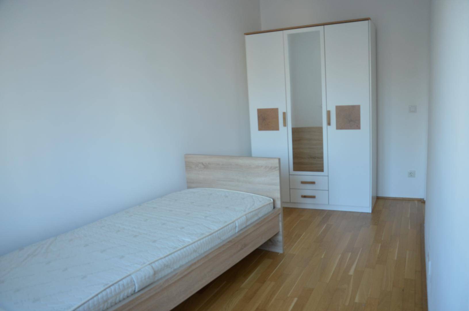 Helles Schlafzimmer mit Einzelbett, Holzparkettboden und einem modernen Kleiderschrank.