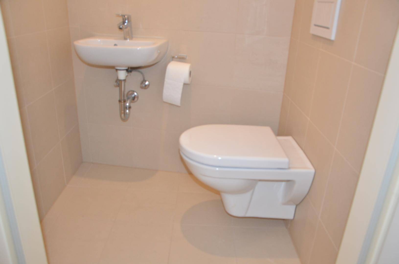 Modernes Gäste-WC mit wandhängender Toilette, kleinem Waschbecken und hellen Fliesen.