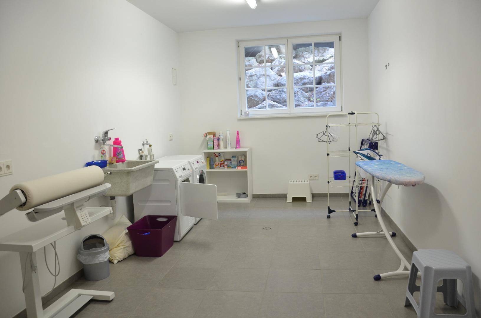 Funktionaler Hauswirtschaftsraum mit Waschmaschine, Bügelbrett und Fenster.