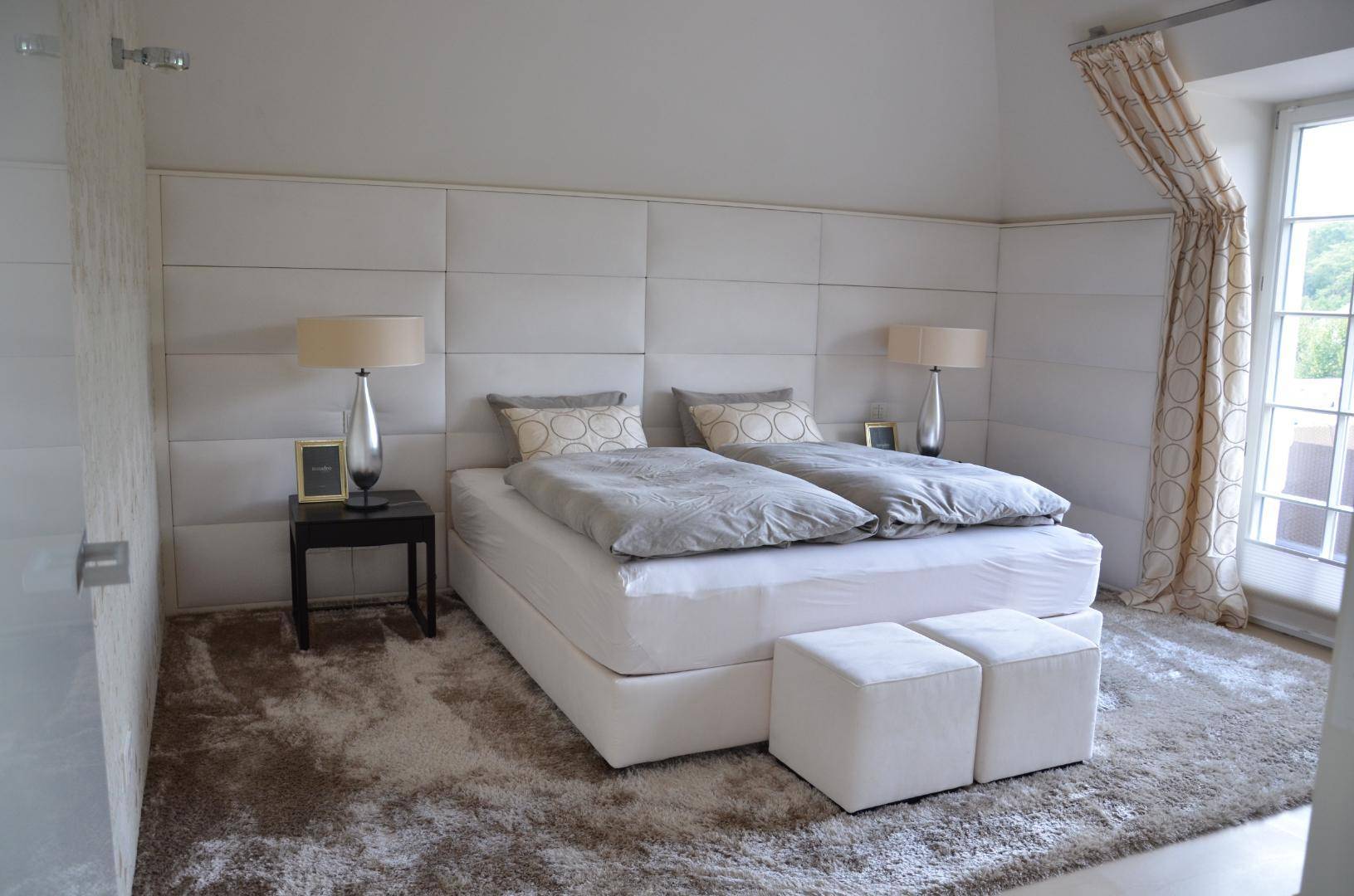 Elegantes Schlafzimmer mit großem Doppelbett, gepolstertem Kopfteil und Teppichboden.