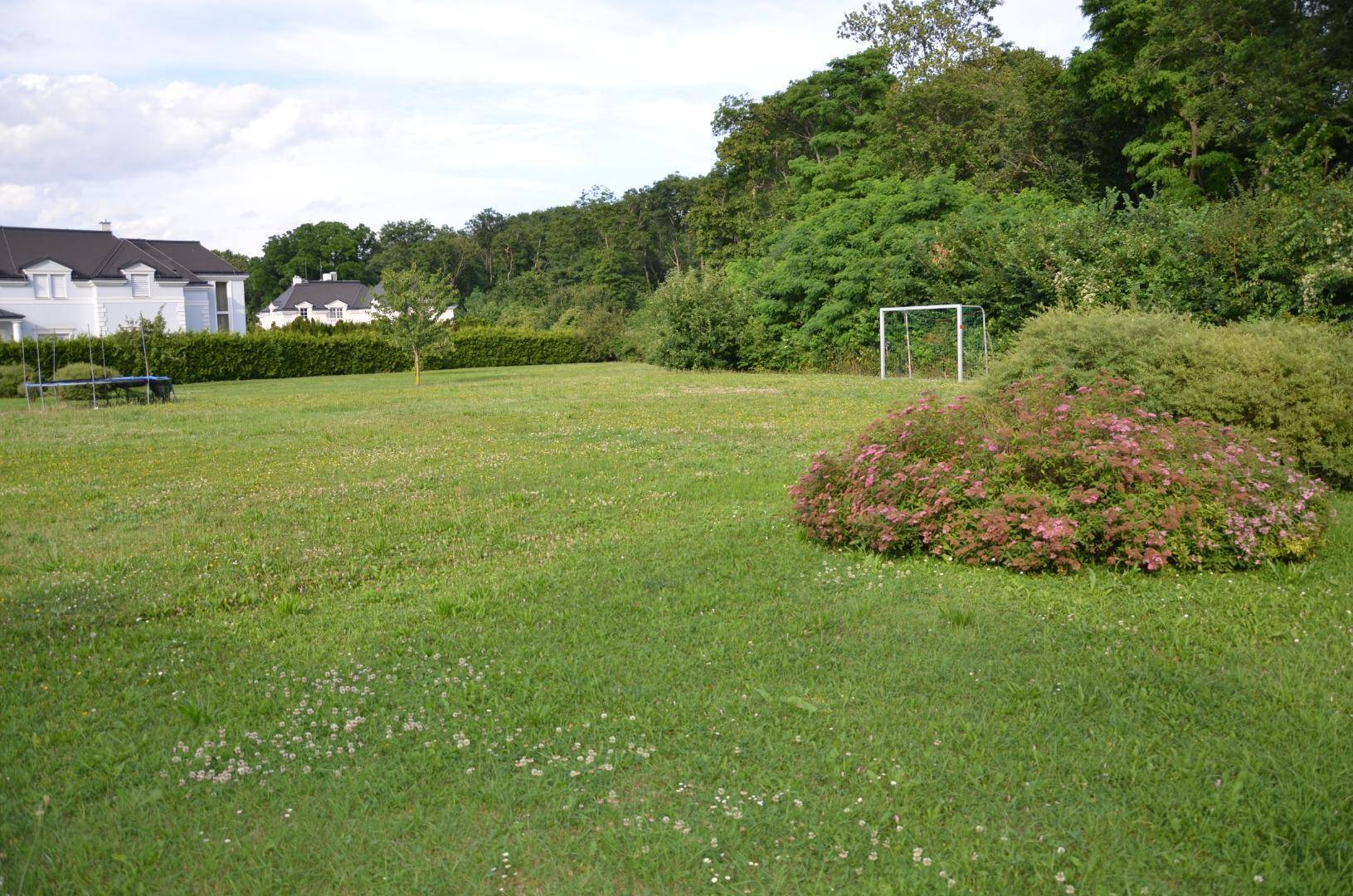Weitläufiger Rasenbereich mit Fußballtor und üppiger Vegetation im Hintergrund.