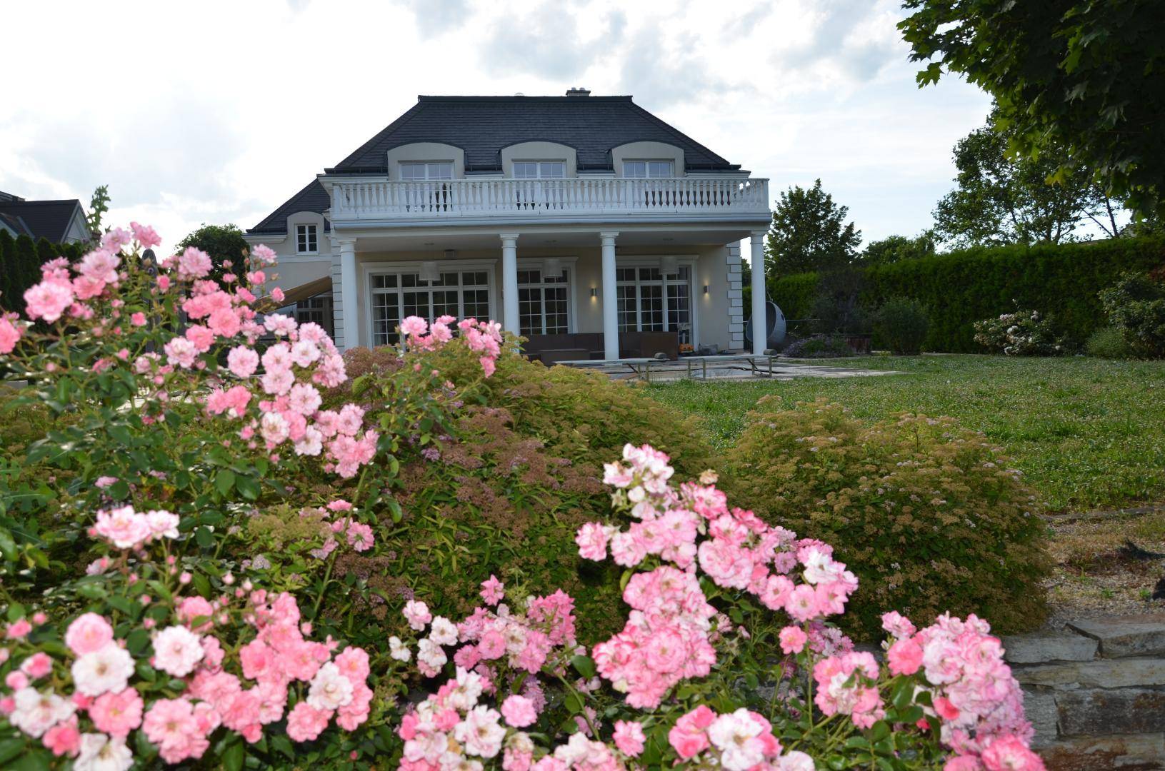 Malerischer Garten mit blühenden Rosen und Blick auf die elegante Villa mit Terrasse.