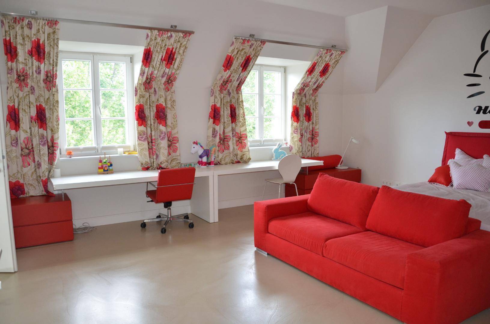 Farbenfrohes Kinderzimmer mit rotem Sofa, Schreibtisch und großen Fenstern.