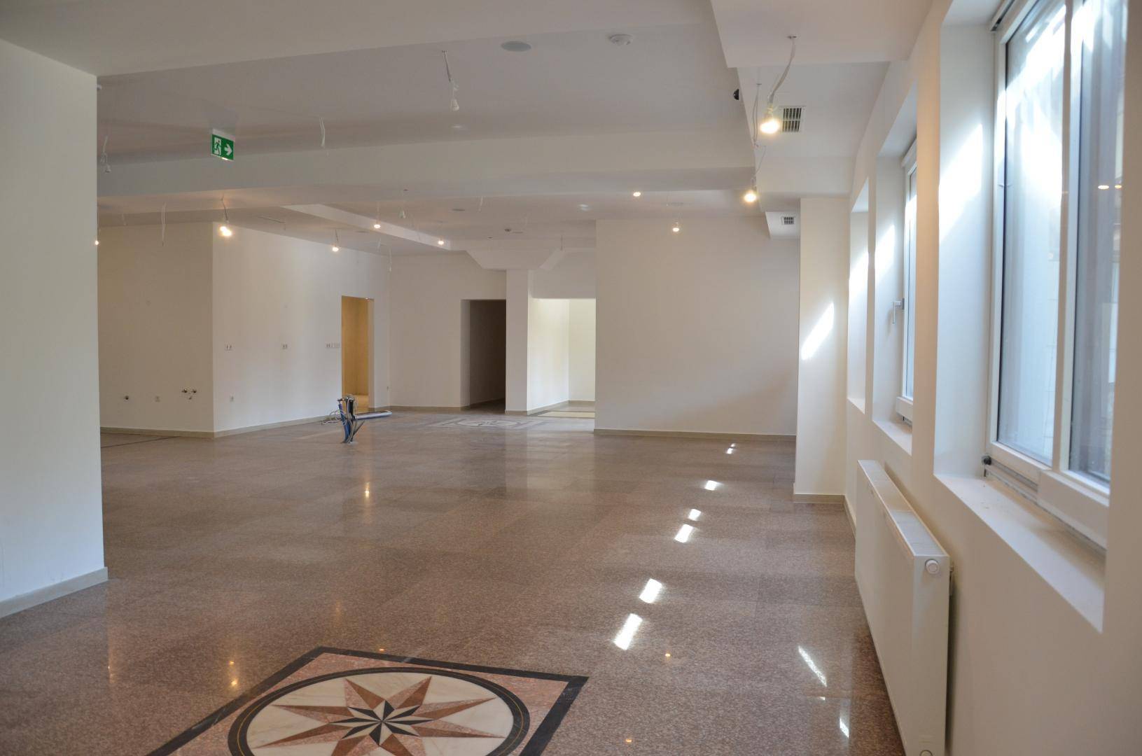 Großer, offener Gewerberaum mit vielen Fenstern, Terrazzoboden und hoher Decke, bereit zur Gestaltung.