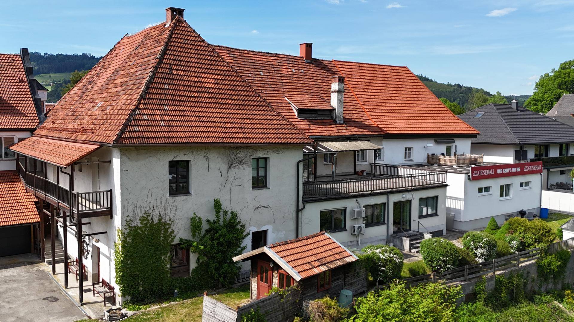 Historisches Gebäude mit rotem Ziegeldach, mehreren Balkonen und einem kleinen Gartenschuppen.