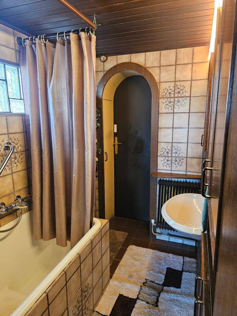 Badezimmer im 80er-Jahre-Stil mit Badewanne, Fliesen und Holzdecke.