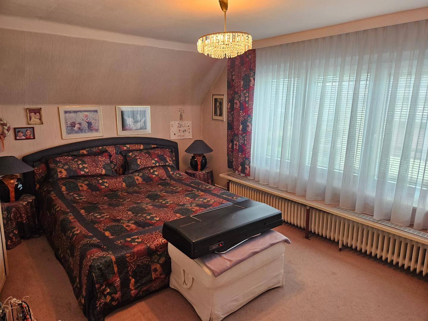 Schlafzimmer im Dachgeschoss mit großem Fenster, Teppichboden und einem Kronleuchter.