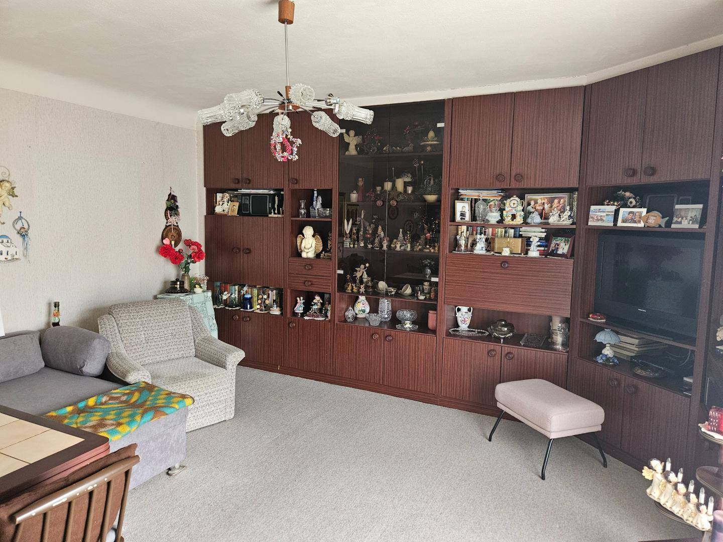 Wohnzimmer mit großer Schrankwand, Teppichboden und gemütlichen Sitzmöbeln in warmen Tönen.