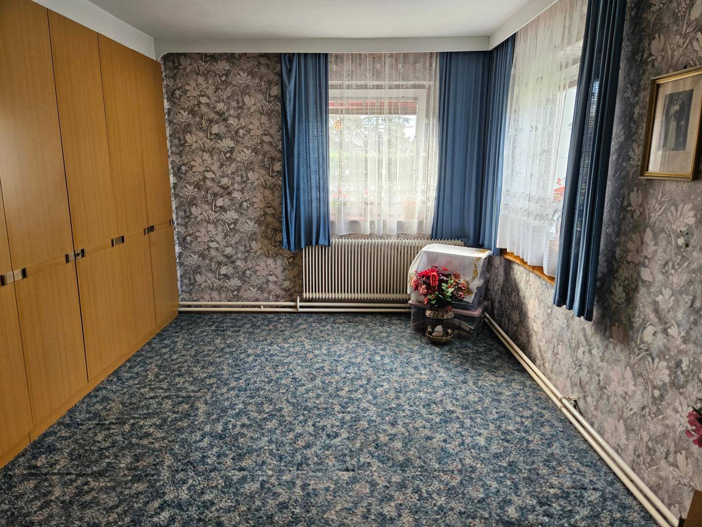 Schlafzimmer mit gemusterter Tapete, blauem Teppichboden und Einbauschränken aus Holz.