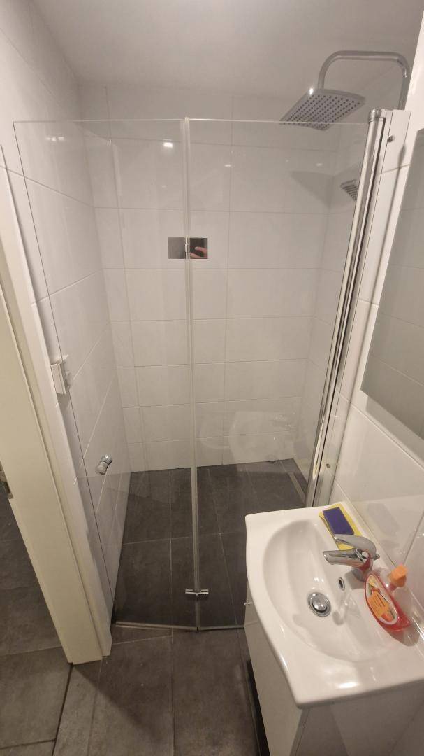Modernes Badezimmer mit weiß gefliesten Wänden, dunklem Boden und einer Glasdusche.