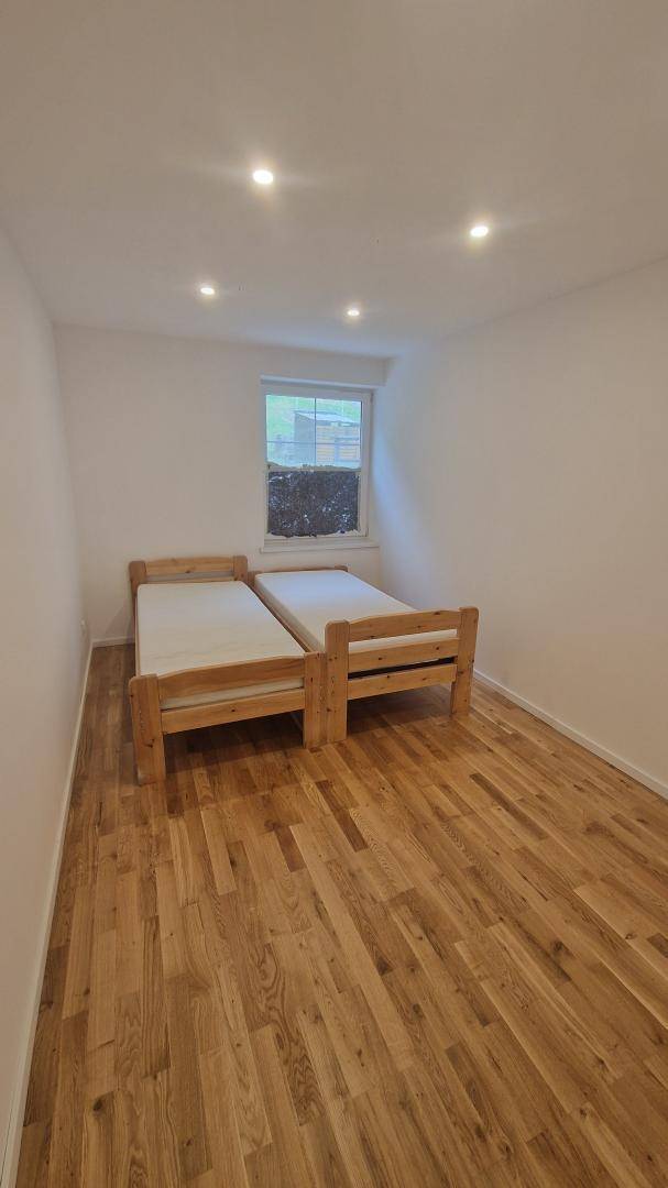 Schlafzimmer mit zwei Einzelbetten aus Holz, Holzboden und einem kleinen Fenster.