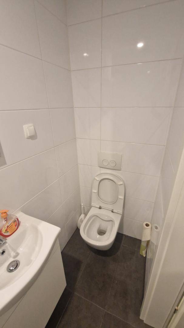 Kleines WC mit weiß gefliesten Wänden, dunklem Boden und einem wandhängenden WC.