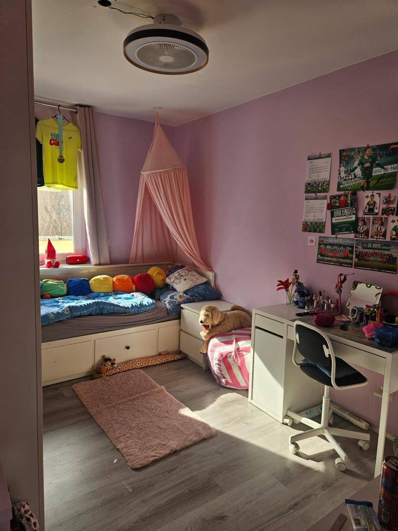 Kinderzimmer mit rosa Wänden, Bett mit Stauraum und Schreibtisch.