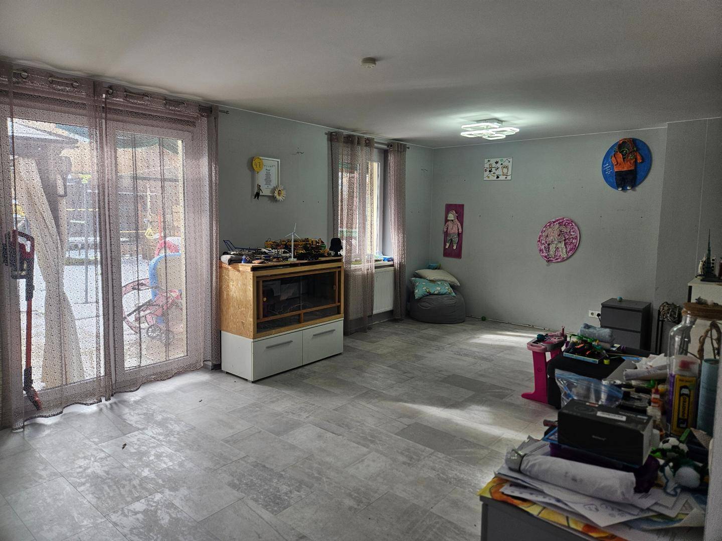 Geräumiges Wohnzimmer mit Fliesenboden und großen Fenstern für viel Tageslicht.