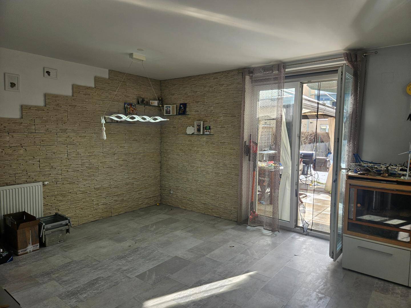 Helles Wohnzimmer mit Steinwand-Akzent, Fliesenboden und Zugang zur Terrasse.