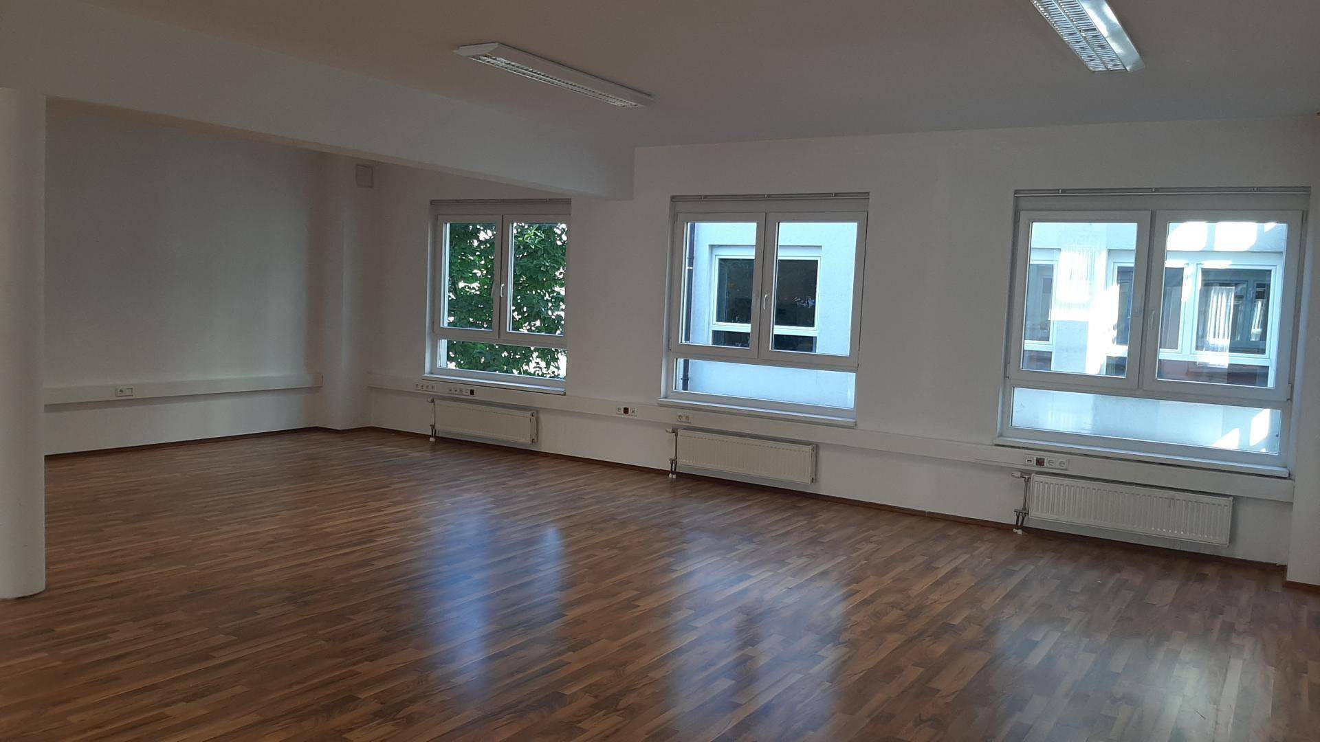 Heller Büroraum mit Holzparkett und mehreren Fenstern, die eine angenehme Arbeitsatmosphäre schaffen.