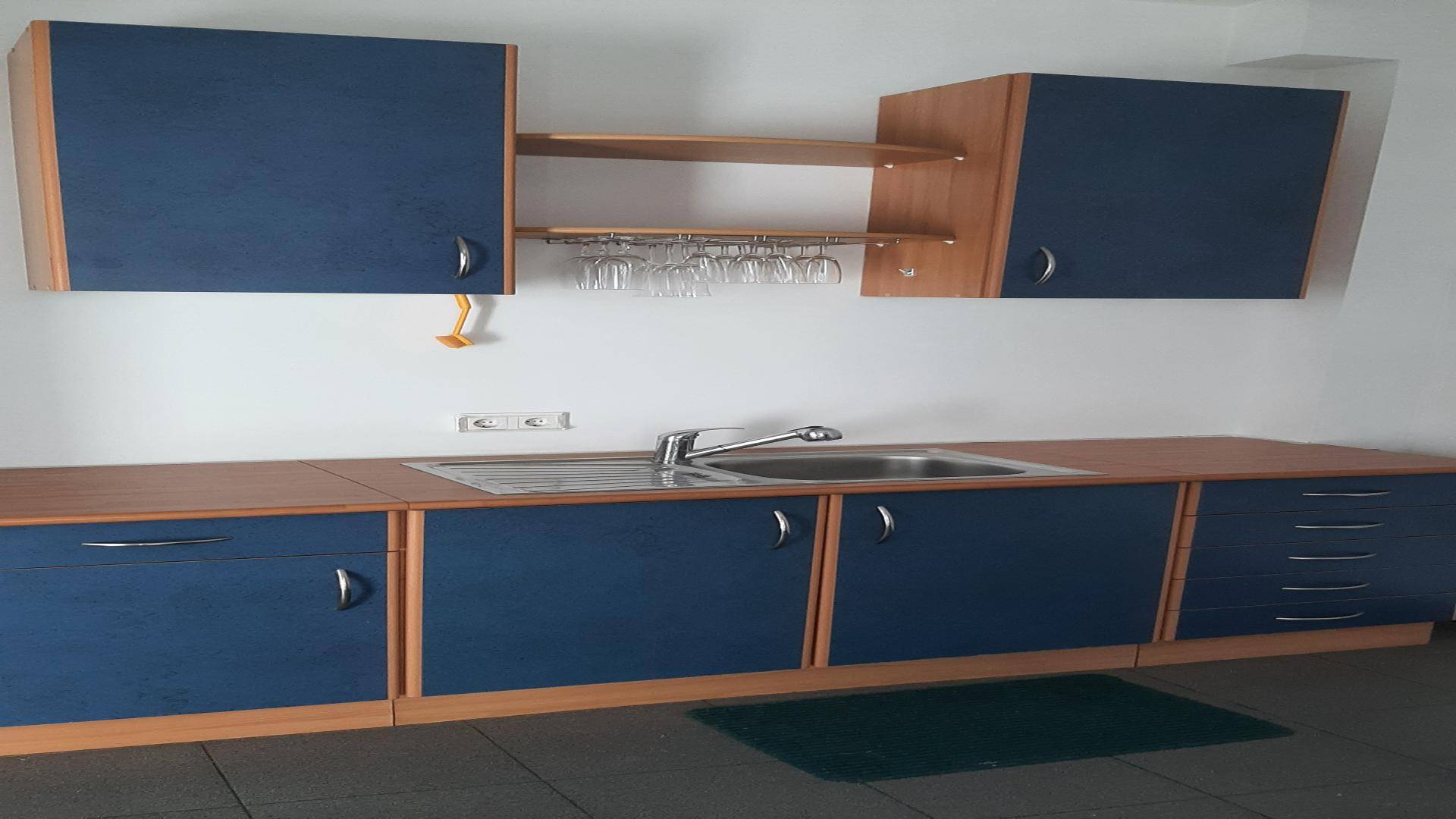 Funktionale Teeküche mit blauen Schränken, Holztheke und Spülbecken, ideal für kurze Pausen.