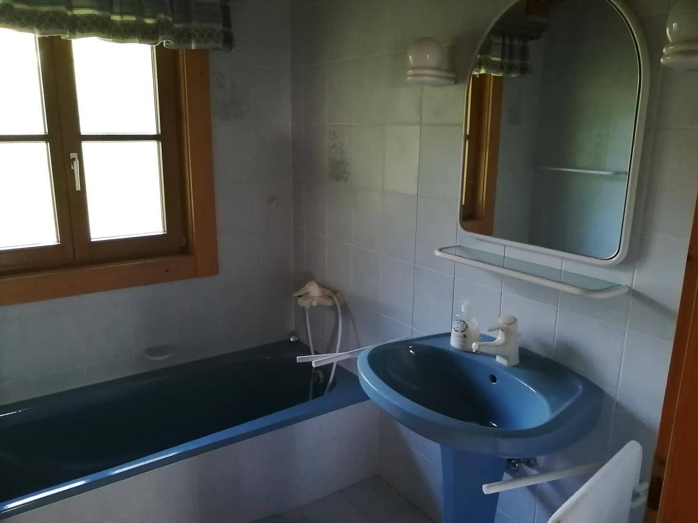 Badezimmer im Stil der 80er Jahre mit blauen Sanitärobjekten, einer Badewanne und hellblauen Fliesen.