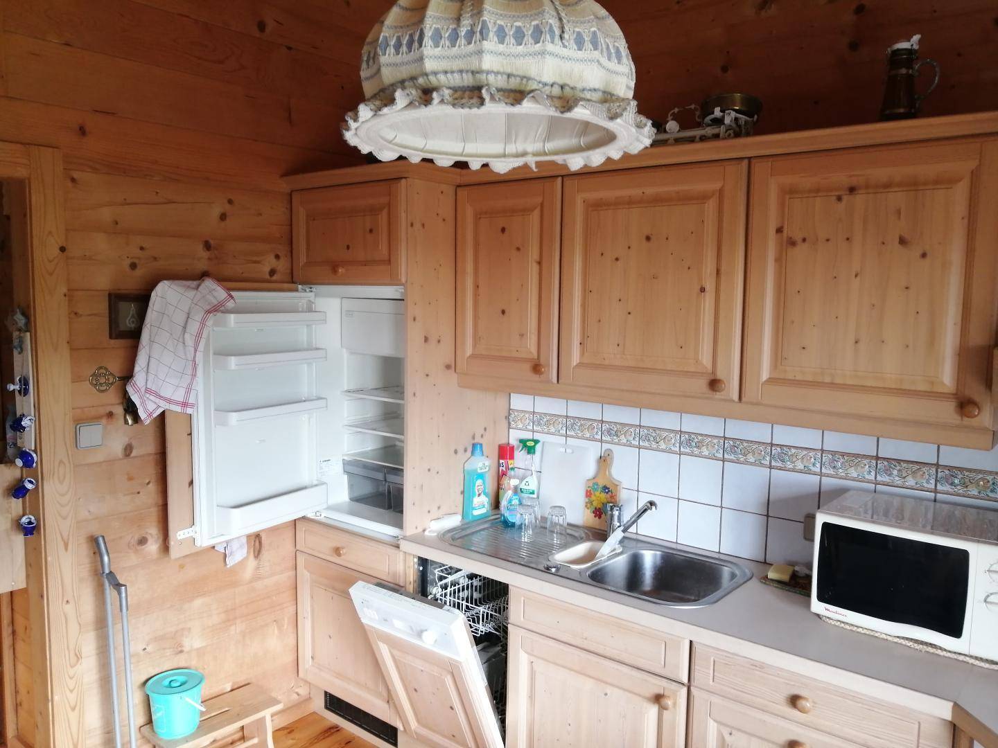 Funktionale Küche mit hellen Holzschränken, Spüle, Mikrowelle und einem offenen Kühlschrank.