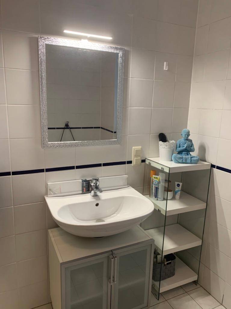 Badezimmer mit weißen Fliesen, modernem Aufsatzwaschbecken und beleuchtetem Spiegel.