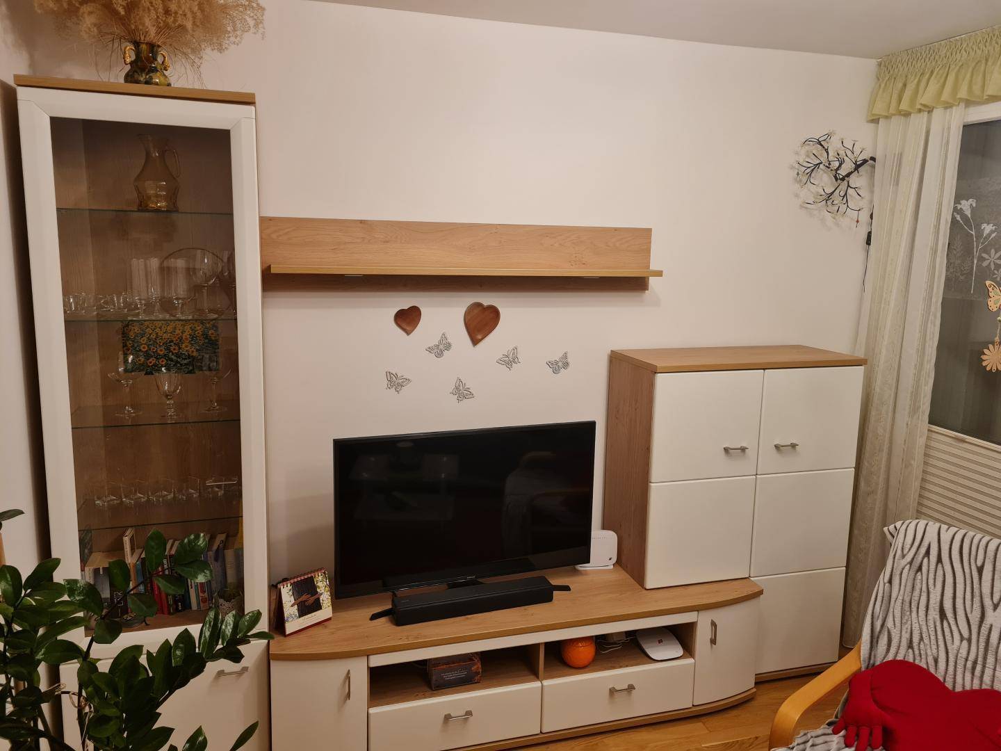 Wohnzimmerbereich mit TV-Möbeln, Vitrine und dekorativen Schmetterlingen an der Wand.