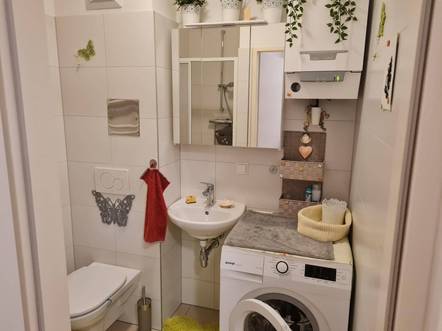 Kleines Badezimmer mit WC, Waschbecken, Waschmaschine und Wandfliesen.