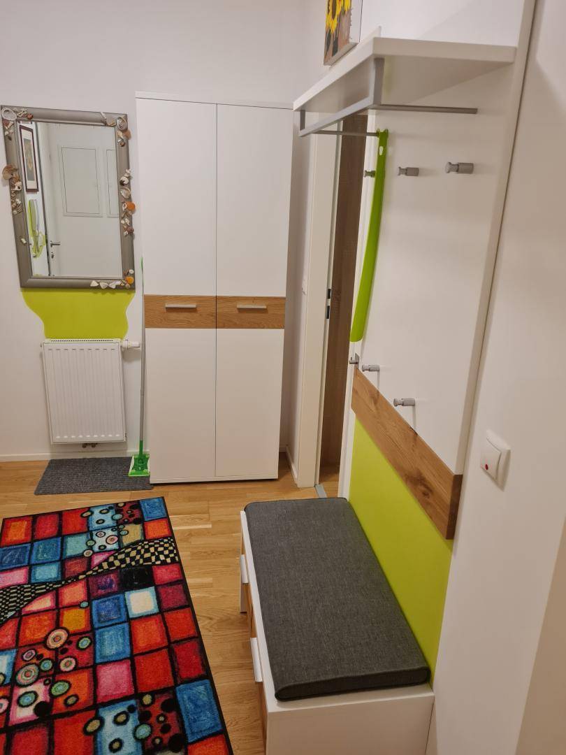 Heller Flur mit Garderobe, Spiegel und farbenfrohem Teppich.