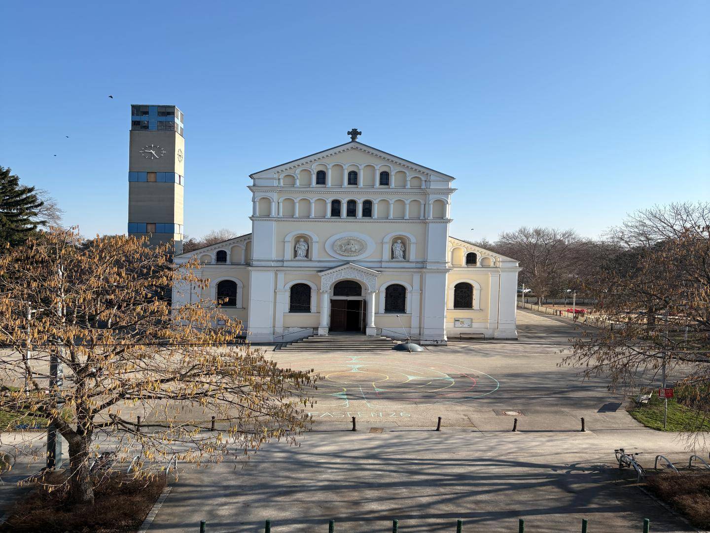 Historische Kirche mit Glockenturm und großem Vorplatz unter blauem Himmel.