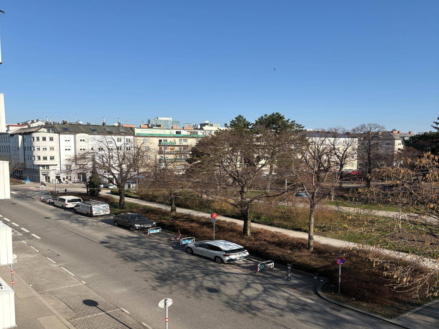 Blick auf eine ruhige Straße mit parkenden Autos und Bäumen.