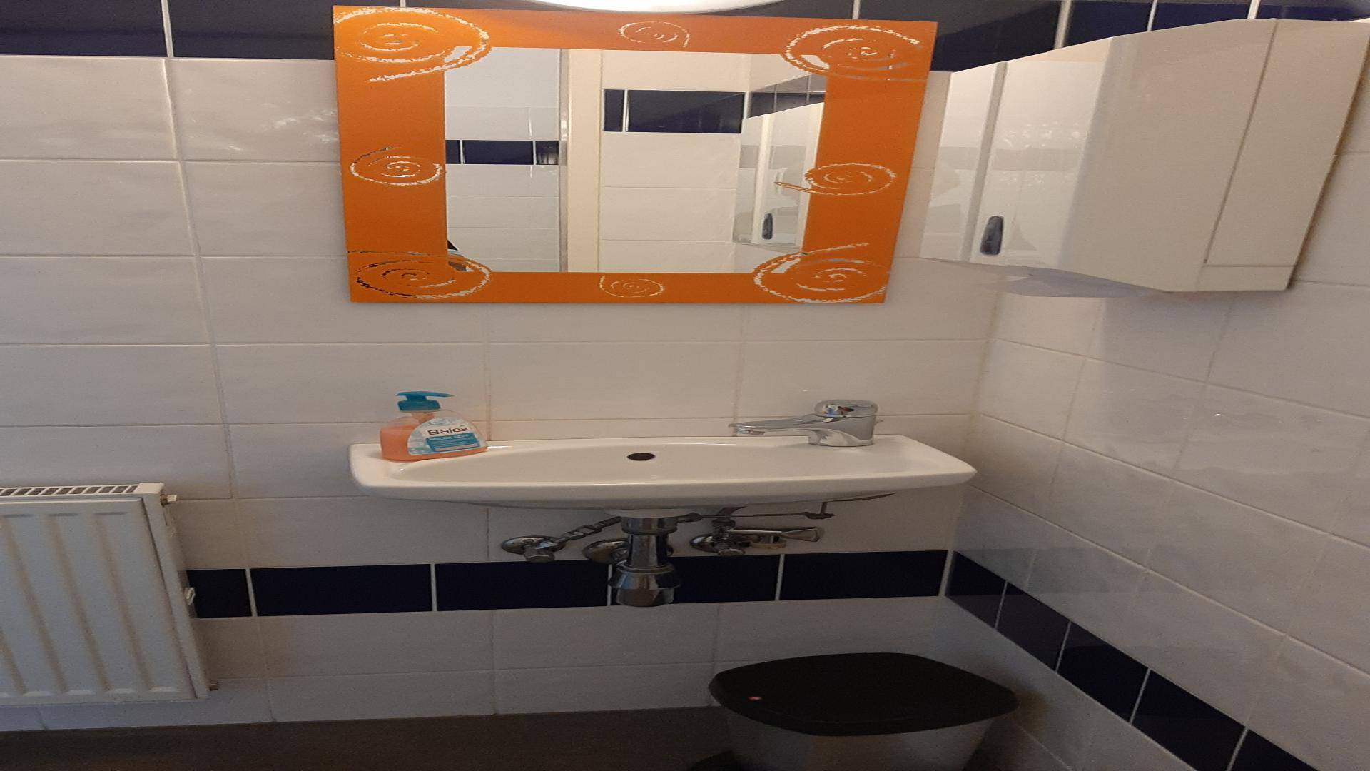 Modern gefliestes Badezimmer mit Waschbecken, Spiegel und Heizkörper, in Weiß und Dunkelblau gehalten.