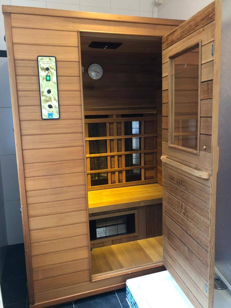 Detailansicht der holzverkleideten Sauna mit offener Tür, die das Innere und die Bänke zeigt.
