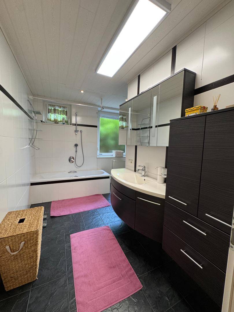 Modernes Badezimmer mit Badewanne, Einzelwaschbecken und dunklen Fliesen, gut beleuchtet.