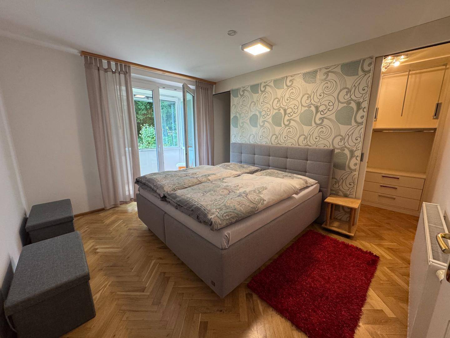 Schlafzimmer mit großem Doppelbett, gemusterter Tapete und direktem Zugang zum Balkon.