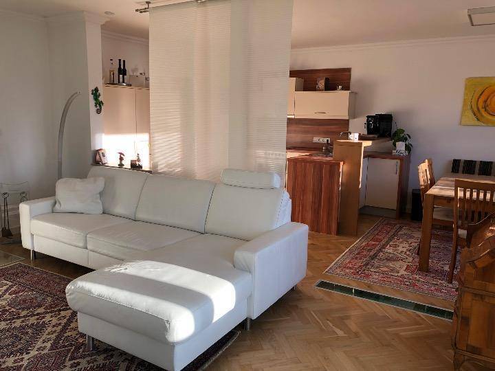 Heller Wohnbereich mit weißem Sofa und offenem Übergang zur Küche, getrennt durch einen Raumteiler.