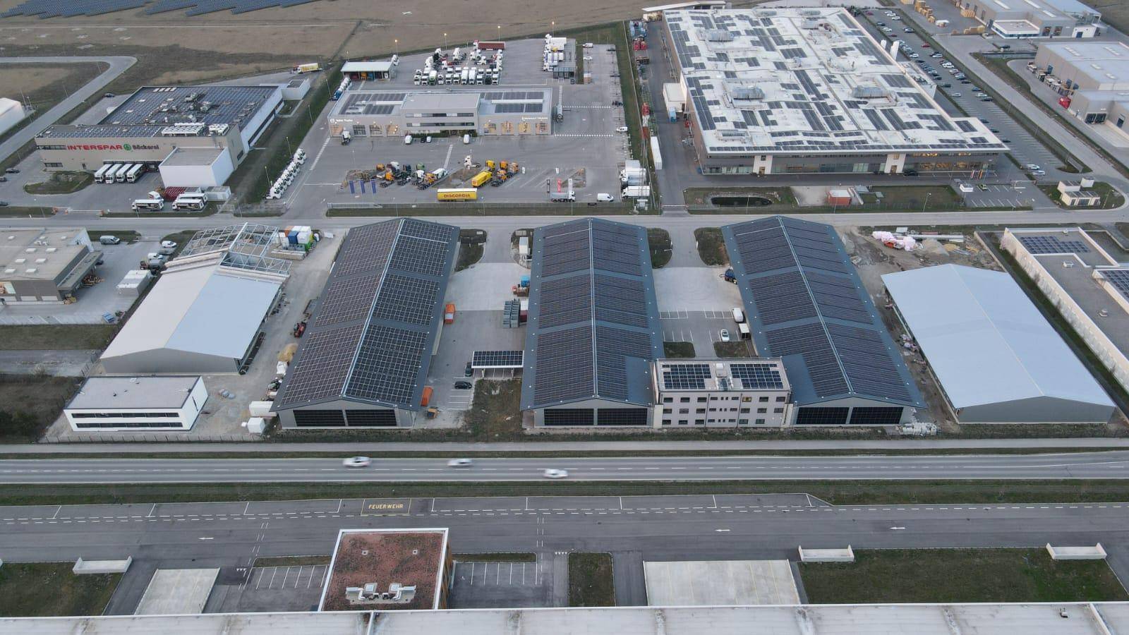 Luftaufnahme eines Industrieparks mit mehreren Gebäuden und Photovoltaikanlagen auf den Dächern.