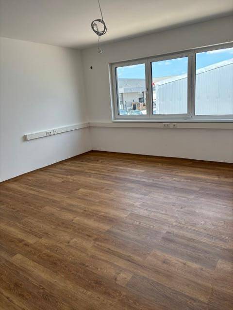Helles Büro mit großen Fenstern, Laminatboden in Holzoptik und weißen Wänden.