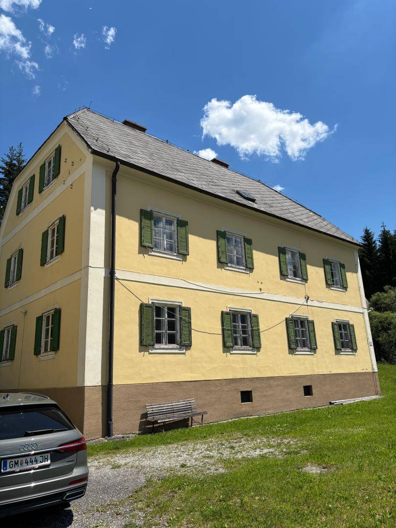 Seitenansicht des historischen Gebäudes mit gelber Fassade, grünen Fensterläden und Blick auf die umliegende Landschaft.