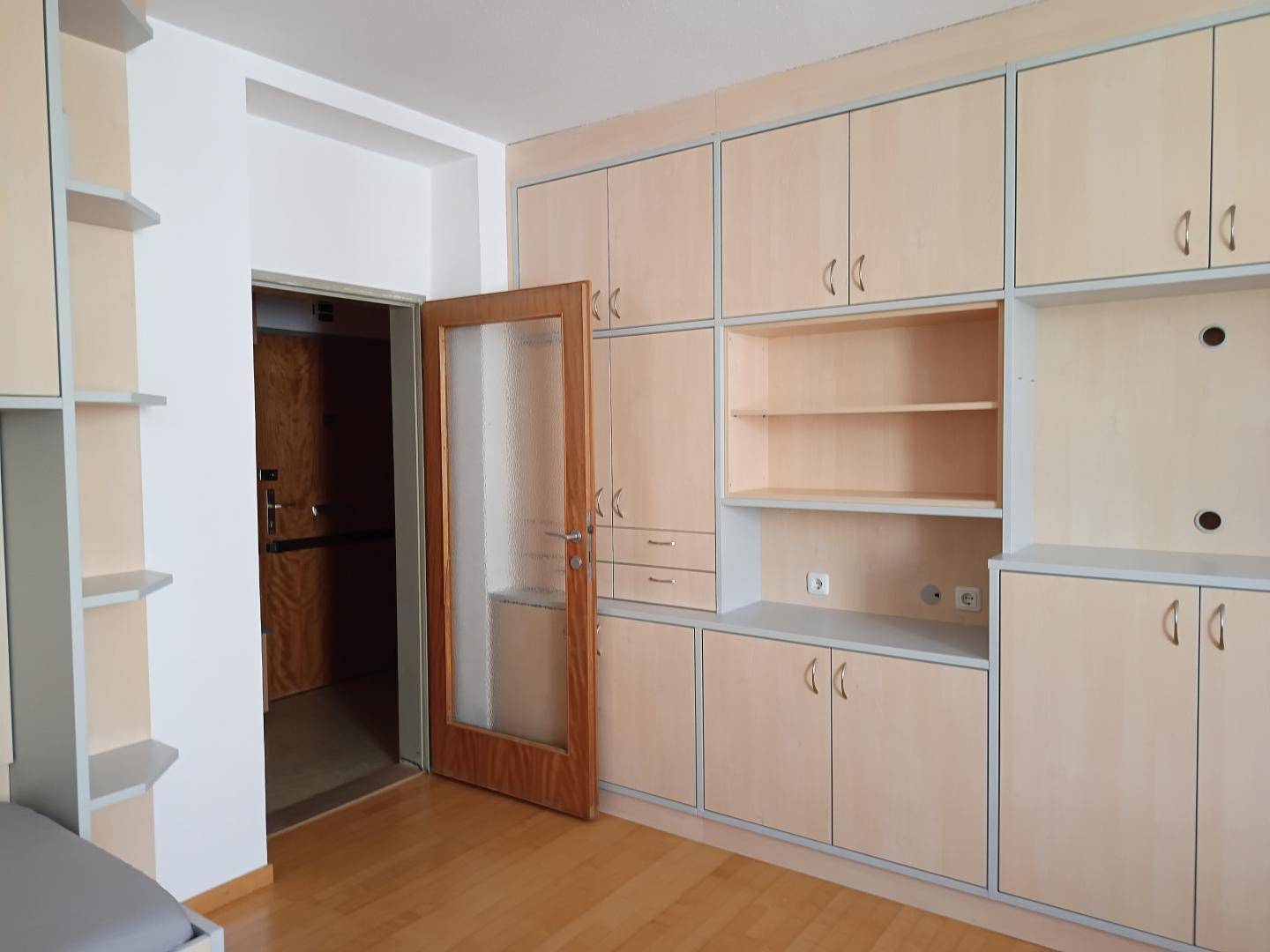 Große Einbauschrankwand mit hellem Holz und einer Tür, die zum Eingangsbereich führt.