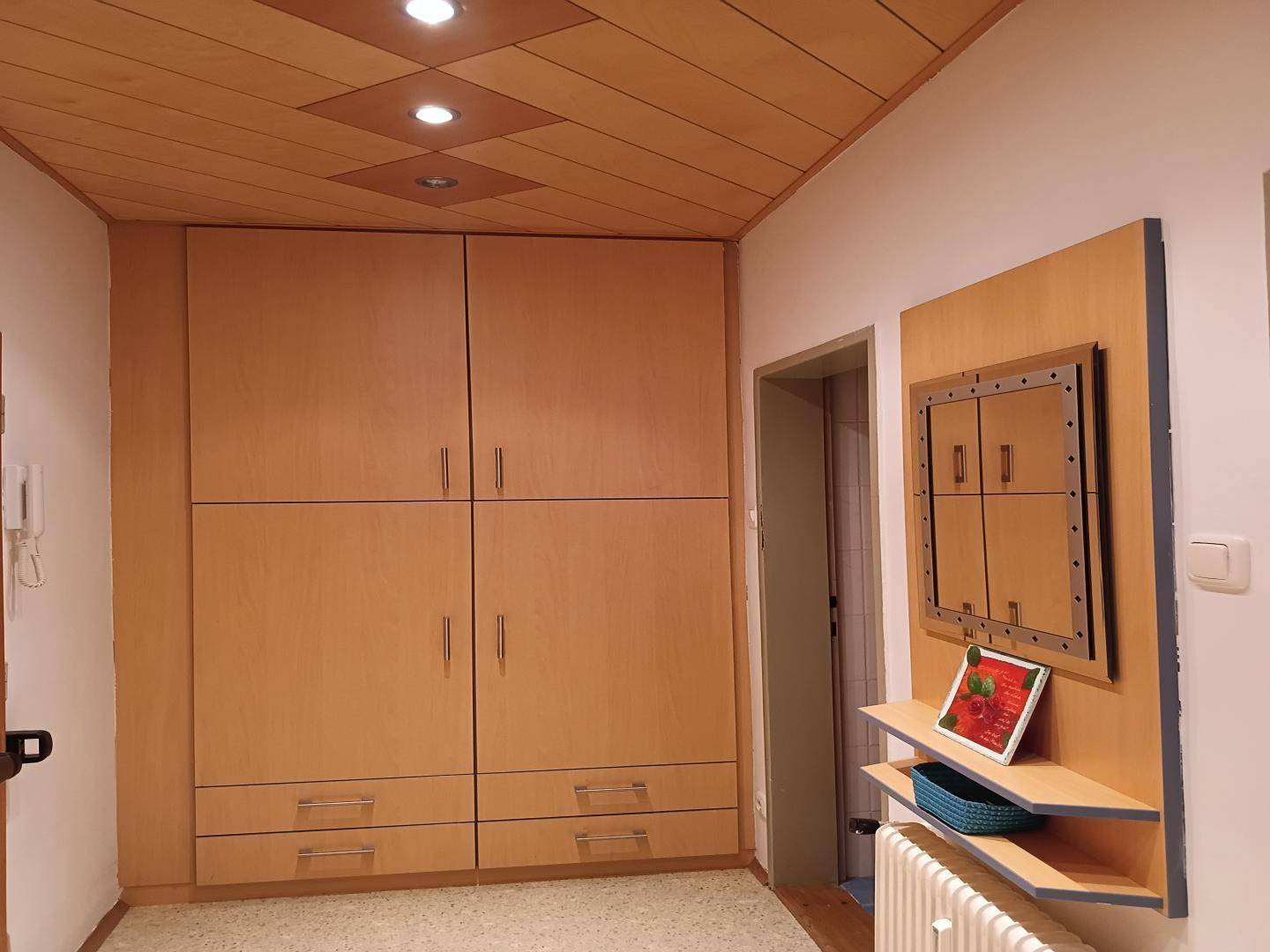 Flur mit großem Einbauschrank, Holzdecke und dekorativer Wandverkleidung mit Ablageflächen.